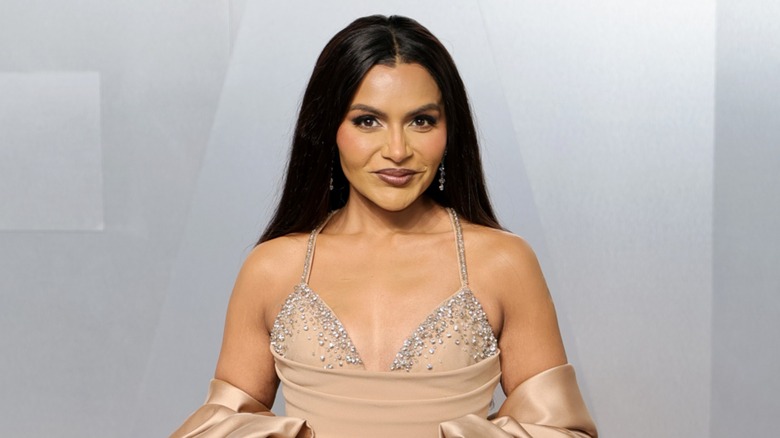 Mindy Kaling wearing a bedazzled, nude dress in front of a silver background