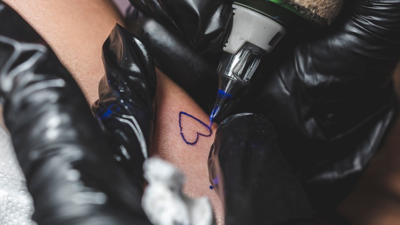 Artist drawing a small heart tattoo