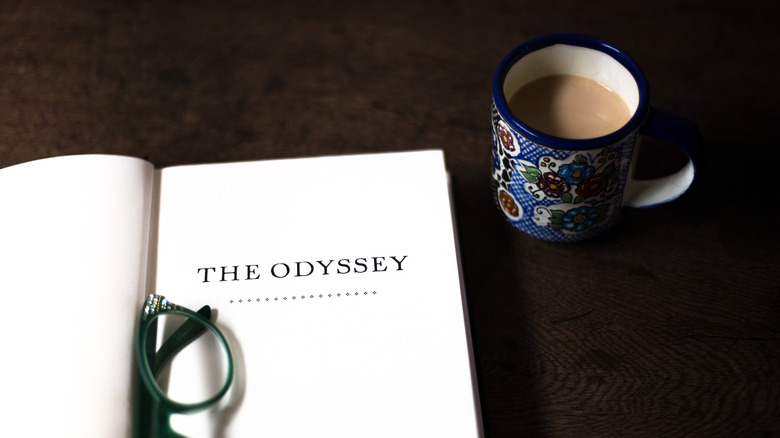 The Odyssey book open on a table with reading glasses in the spine and coffee to the right