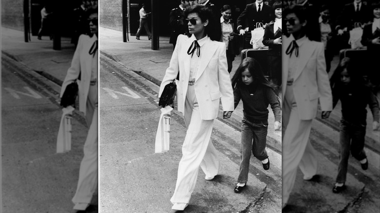 Bianca Jagger walking across the road in a white suit with a black bow tie