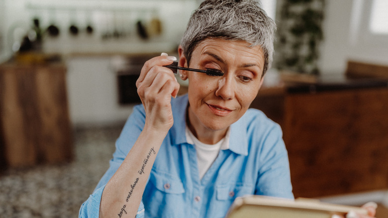 An older woman with arm tattoo applying mascara