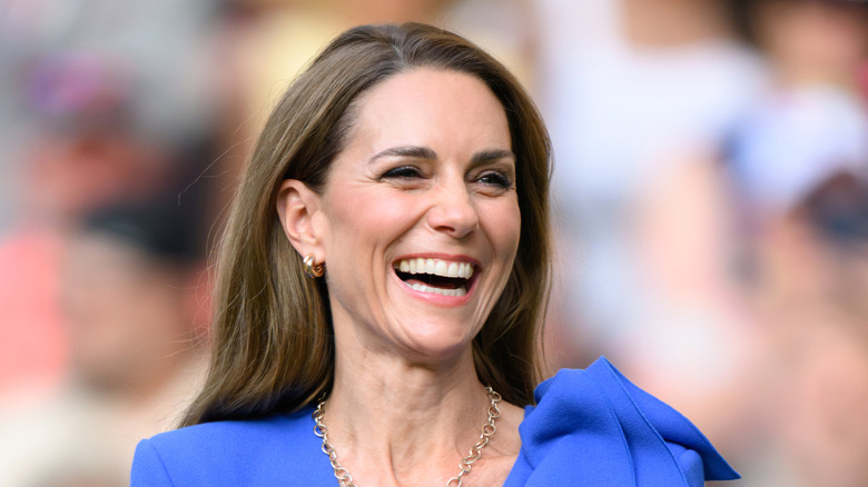 Kate Middleton with dark brown hair laughing in a blue dress