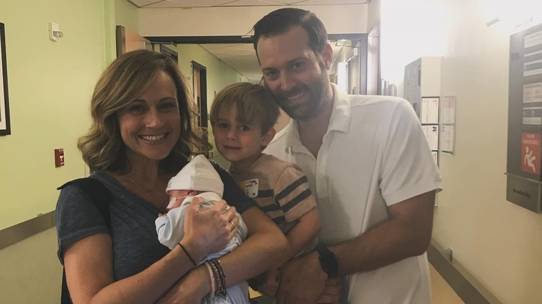 Nikki DeLoach smiling in a hospital hallway with her two sons and husband