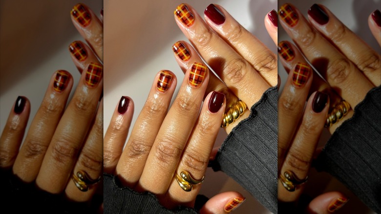 Two overlapping hands showing nails with solid berry polish and plaid patterns