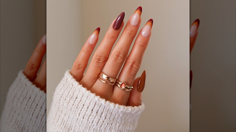 Single hand showing nail set with several layered French tips in autumn colors