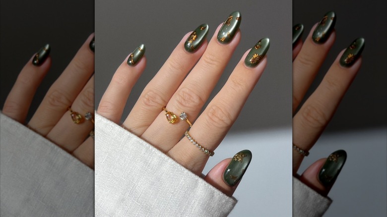 Hand showing olive green nail polish accented with gold foil flakes