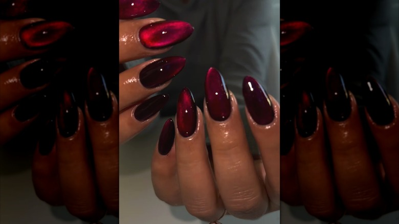 Close-up of two hands showing dark cherry nails with a cat-eye effect