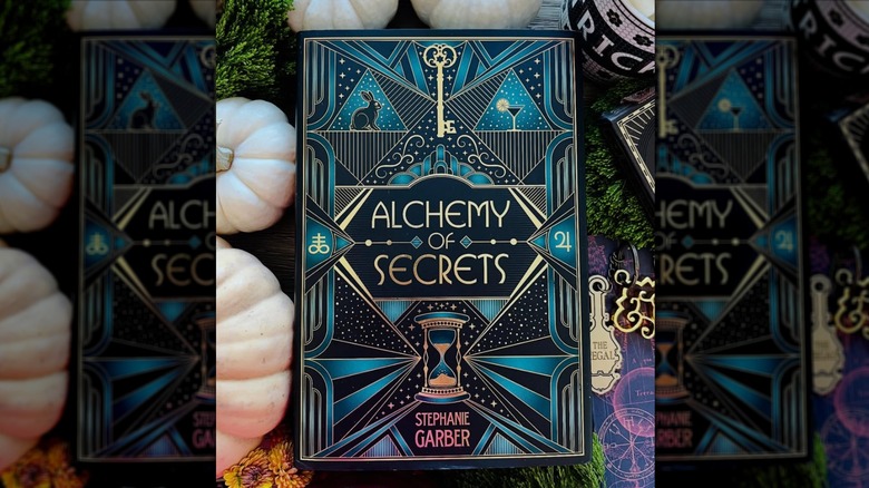 A copy of the book "Alchemy of Secrets" on a table with pumpkins all around it