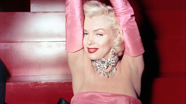 Marilyn Monroe lifting her arms above her head while wearing a bright pink dress and matching gloves