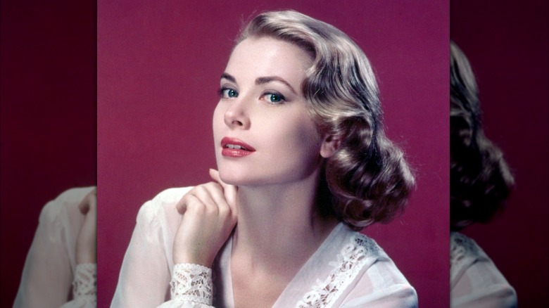 Grace Kelly posing in front of a maroon background wearing a white blouse