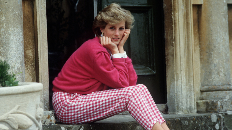 Princess Diana sitting on steps in pink gingham pants and a matching sweater