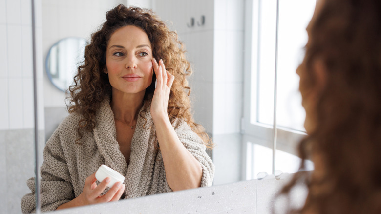 A woman applying skincare to her face in the mirror