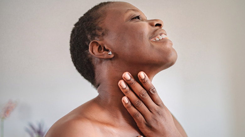 A Black woman applying moisturizer to her neck