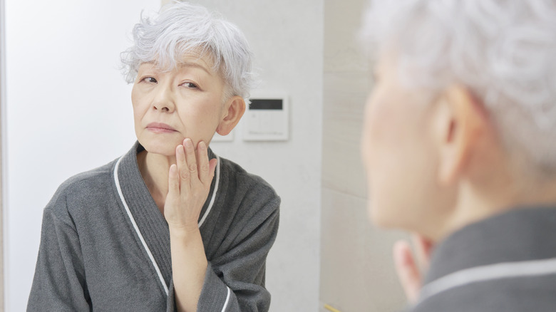 Older woman looking at her skin in the mirror