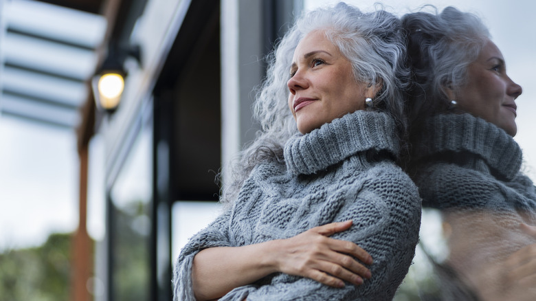 Older woman in a gray sweater leaning against a window
