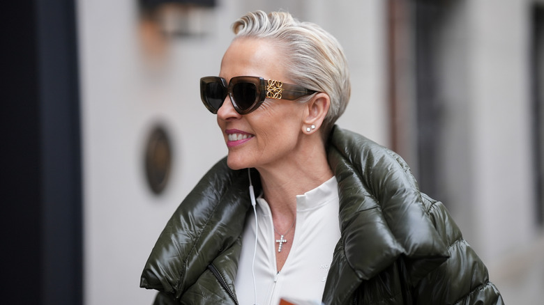 An older woman walking on the street with a puffer jacket and designer sunglasses