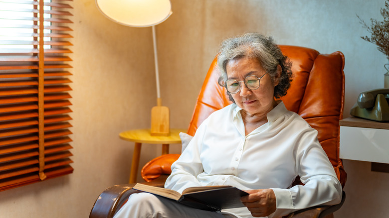 An older woman with glasses sitting in a chair reading