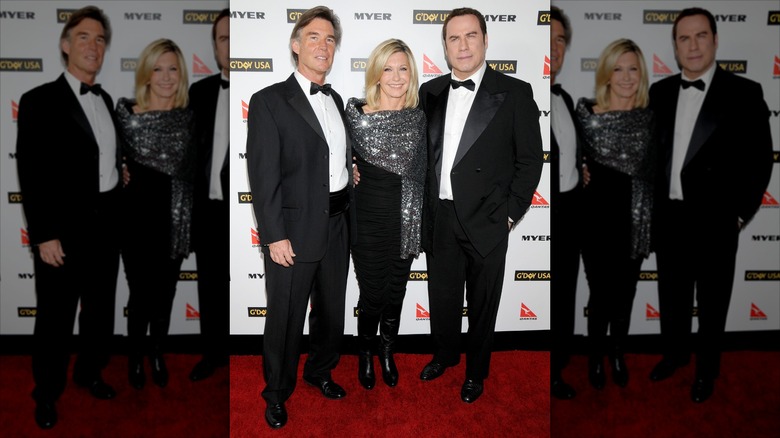 Olivia Newton-John posing on the red carpet with her husband and John Travolta in a black dress and sparkly wrap