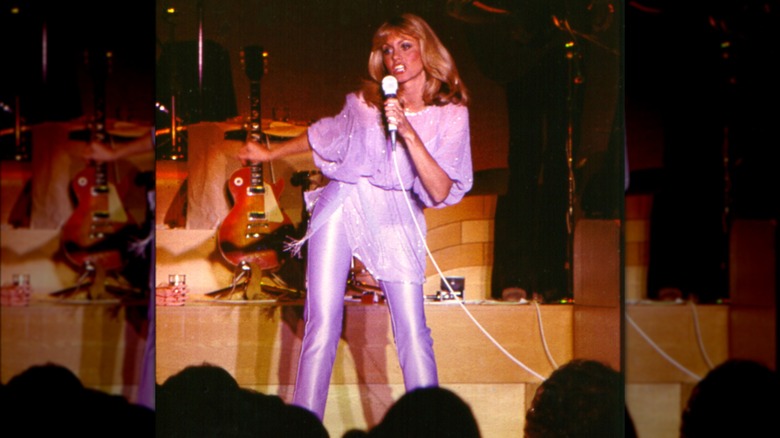 Olivia Newton-John performing on stage in a monochrome lilac outfit in 1983
