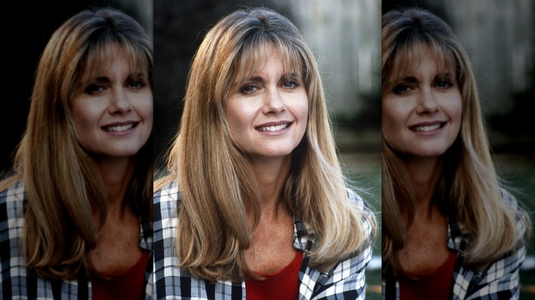 Olivia Newton-John smiling while wearing a plaid shirt in 1990