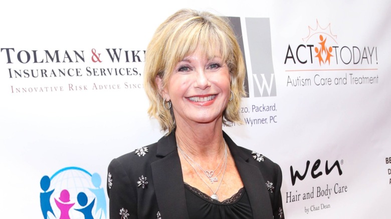 Olivia Newton-John smiling on the red carpet in 2017 wearing a bedazzled black suit