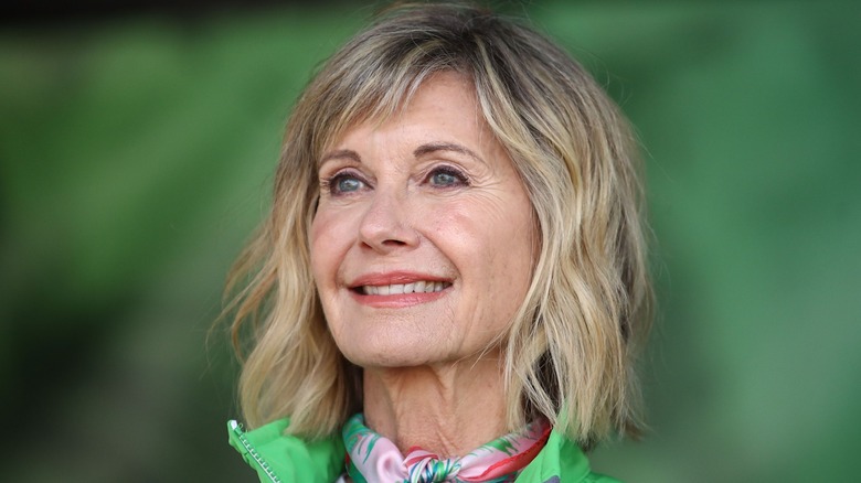 Olivia Newton-John smiling in a photo with a green, blurred background