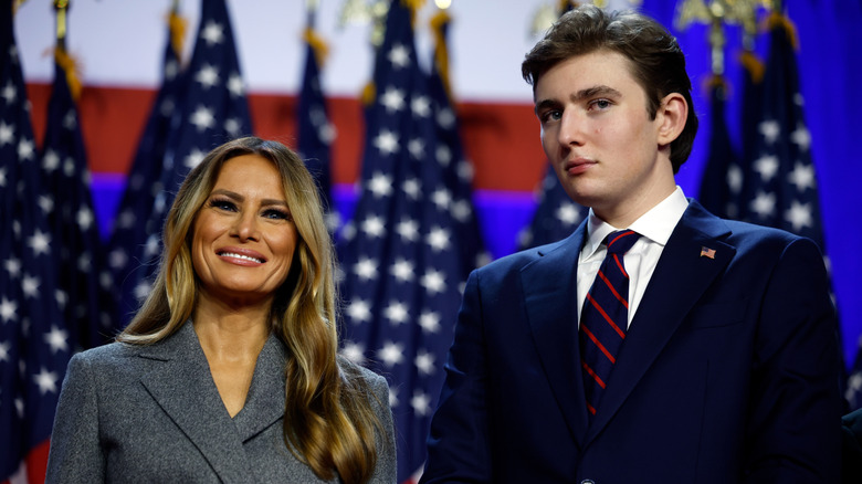 Melania Trump in a grey blazer standing with Barron Trump in a blue blazer at an event