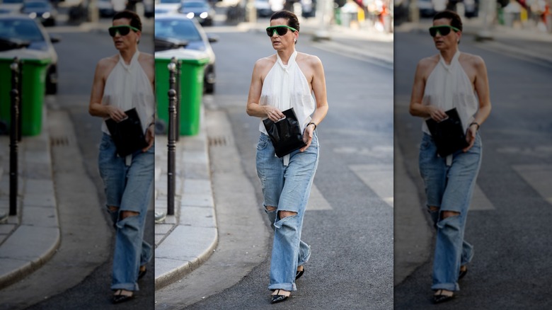A woman in a white halter top and ripped jeans