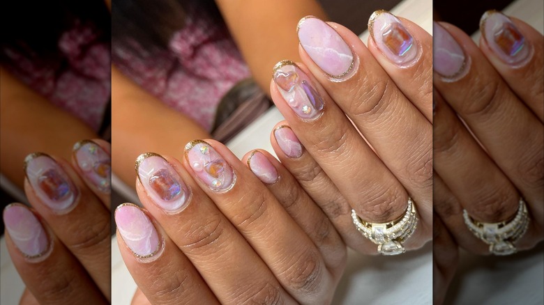 Two hands showing a pink, opal-inspired nail design decorated with nail charms