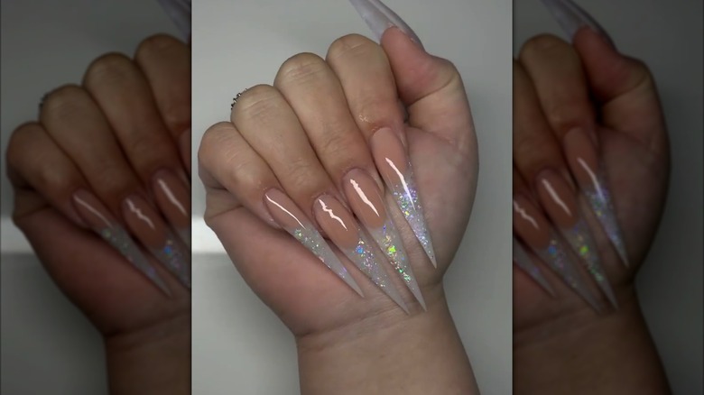 A folded hand showing long, stiletto nails with opal tips