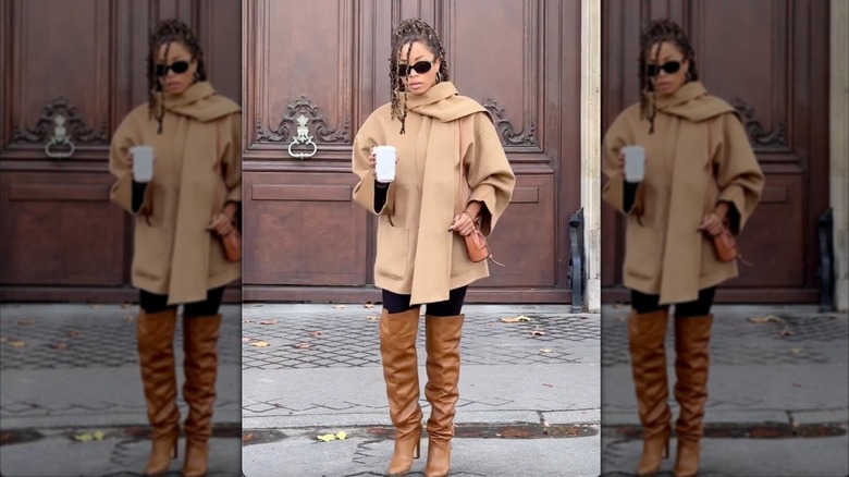 A woman in a camel jacket with slouchy camel boots holding a coffee