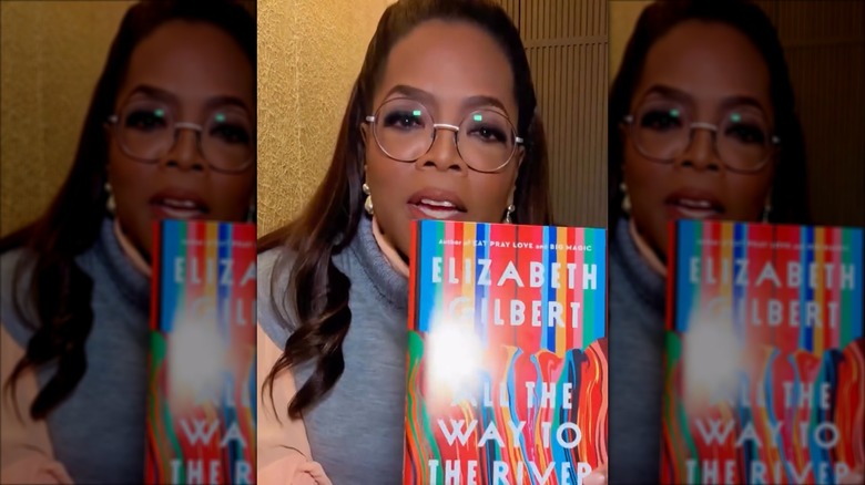 Oprah Winfrey holding a copy of All the Way to the River: Love, Loss, and Liberty, by Elizabeth Gilbert