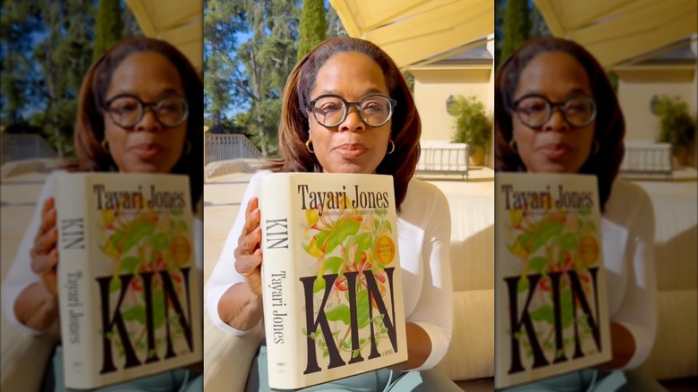 Oprah Winfrey holding up a copy of Kin outdoors