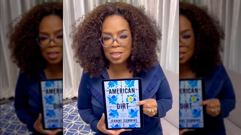 Oprah Winfrey holding an e-reader with the cover of American Dirt by Jeanine Cummins on