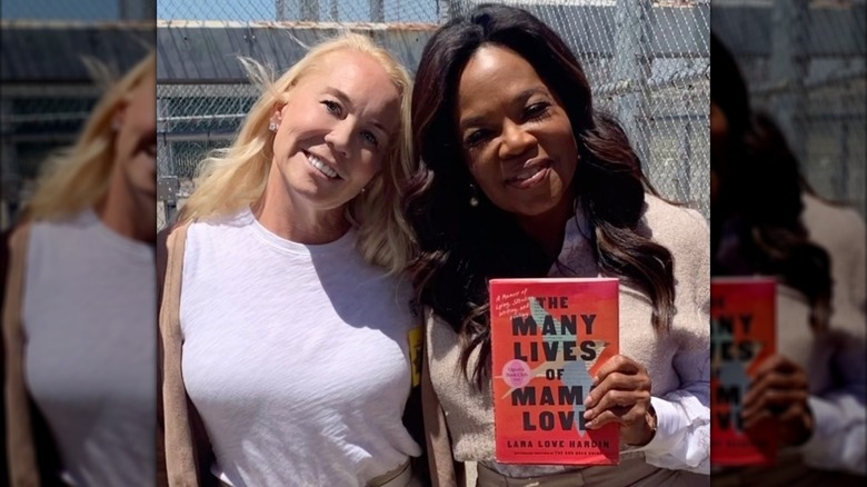 Lara Love Hardin and Oprah Winfrey posing together while Winfrey holds a copy of the book The Many Lives of Mama Love: A Memoir of Lying, Stealing, Writing, and Healing