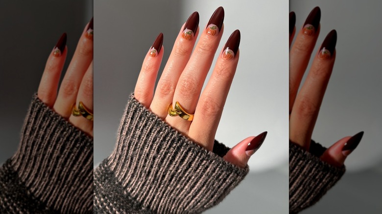 Open hand showing a half-moon French manicure with a hand-painted pumpkin at the base of each nail