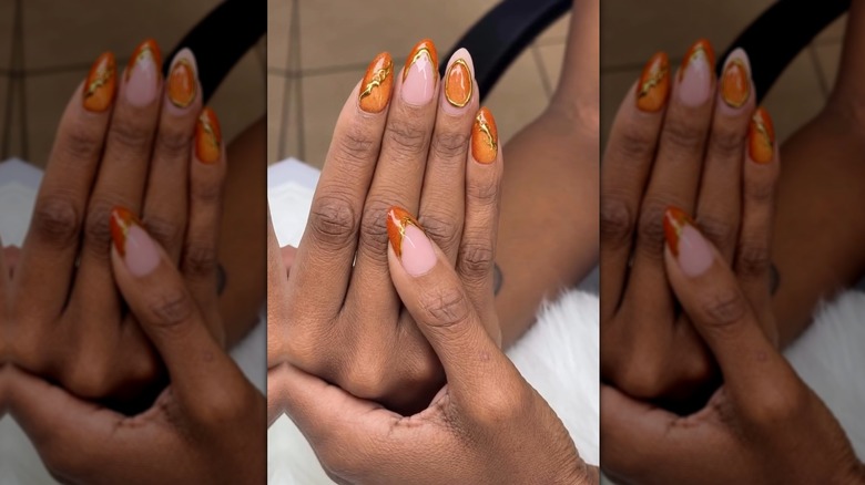 Two hands showing a nail set featuring a orange cat eye and gold accents