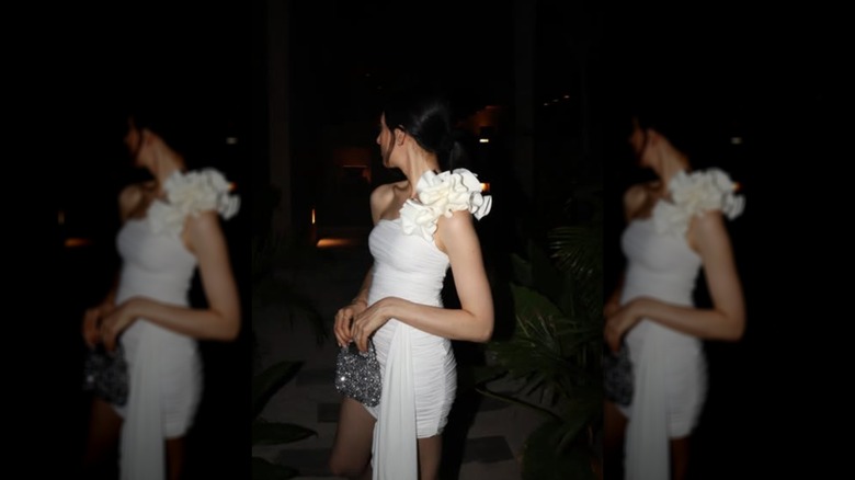 A woman wearing a one-shoulder white dress and holding a tiny sparkling purse