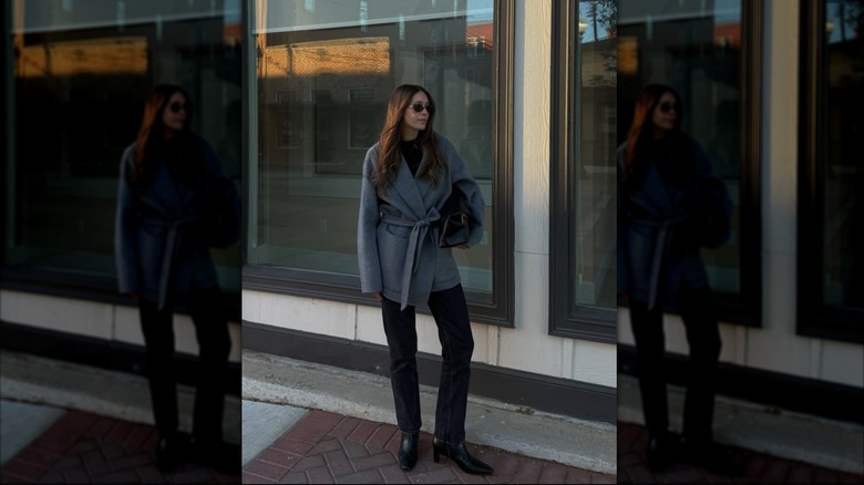 A woman standing in front of a building in black jeans and a wrap coat