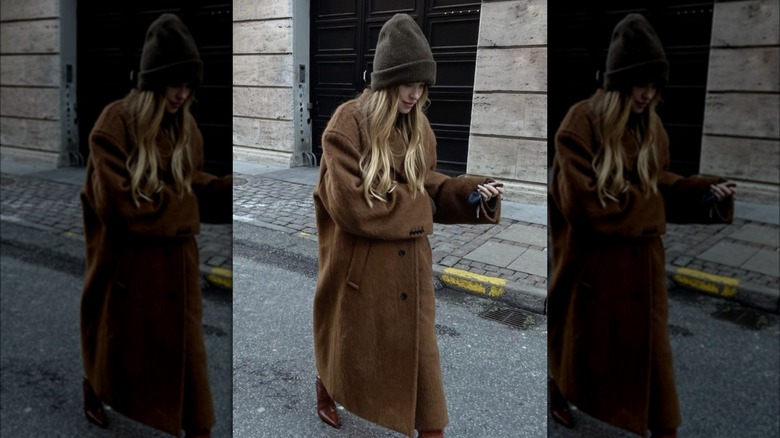 A woman walking down the street in a brown wool trench coat and beanie