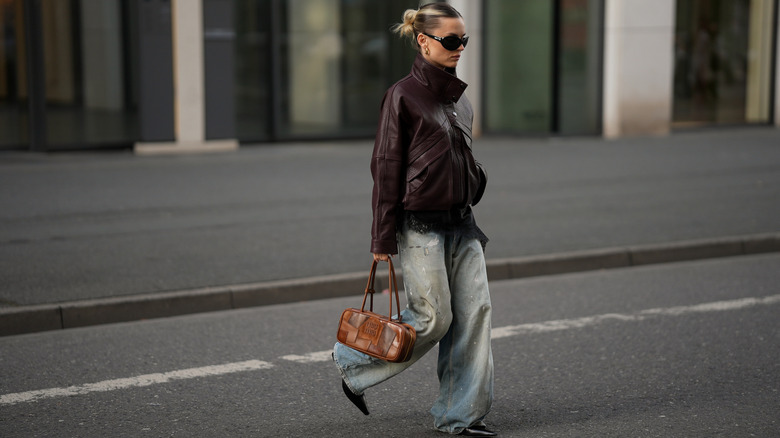 A woman walking in light-wash denim jeans with a brown Miu Miu purse