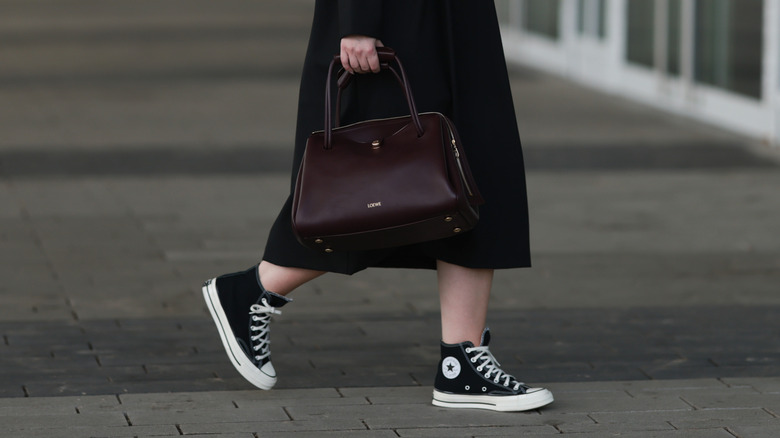 A close up of a woman wearing black high-tops with a brown handbag
