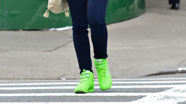A woman wearing neon green sneakers walking across the street