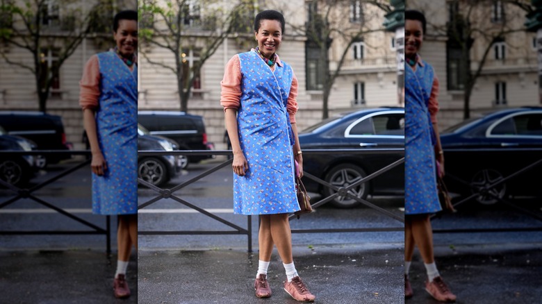 A woman in a blue wrap dress wearing trendy, mauve ballet sneakers