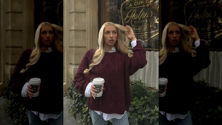 A blonde woman holding a cup of coffee and wearing an oversized burgundy sweater
