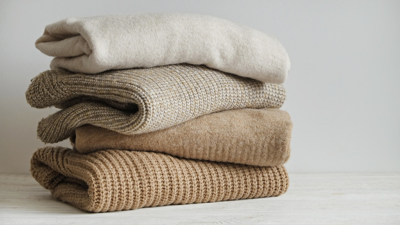 A stack of folded sweaters in oatmeal tones