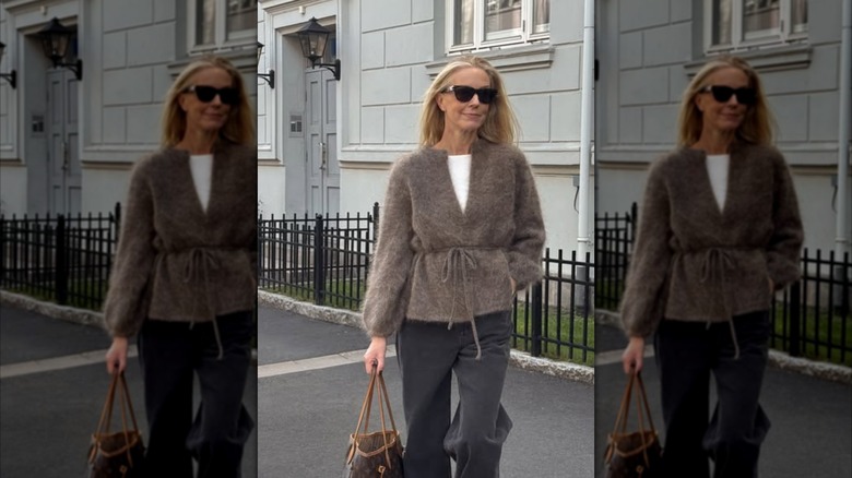 A woman walking and wearing a fuzzy brown cardigan with a belted waist