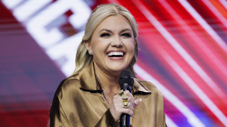 Erika Kirk on stage in a shiny brown shirt holding a microphone
