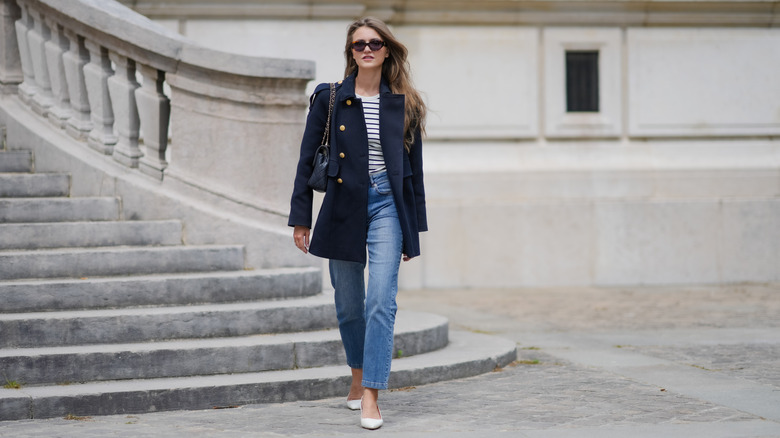 A woman in a navy peacoat with skinny jeans walking outside