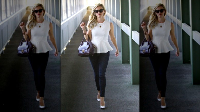 Reese Witherspoon walking down a hallway in a white top and jeans